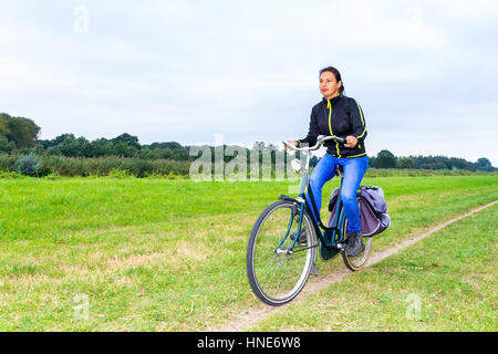 young colombian woman rides bike  on path in european nature