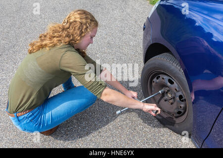 Caucasian teenage girl changing car wheel on streetf Stock Photo