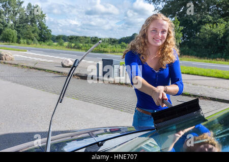 Caucasian teenage girl cleaning car windshield Stock Photo