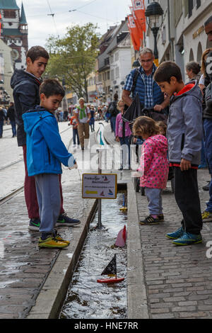 Children sailing toy boats in the Freiburg runnels, Freiburg im Breisgau, Germany Stock Photo