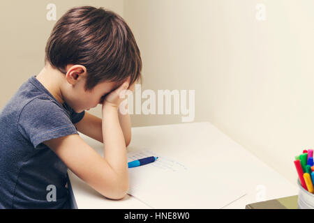 Tired child doing homework at home. The boy fed up and covers his face with hands. Education, school, learning difficulties concept Stock Photo