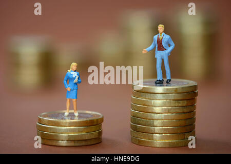 Miniature figures of man and woman on differently high coin piles, symbolic photo for wage inequality, Miniaturfiguren von Mann und Frau auf unterschi Stock Photo