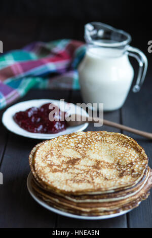 Homemade pancakes with raspberry jam on a dark wooden table. Top view with hands. Shrove Tuesday. Stock Photo