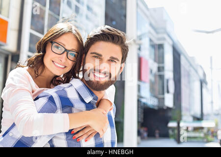 Portrait of happy man giving piggyback ride to woman in city
