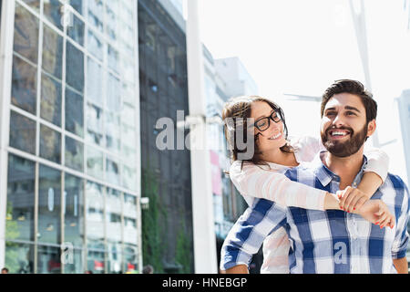 Happy man giving piggyback ride to woman in city