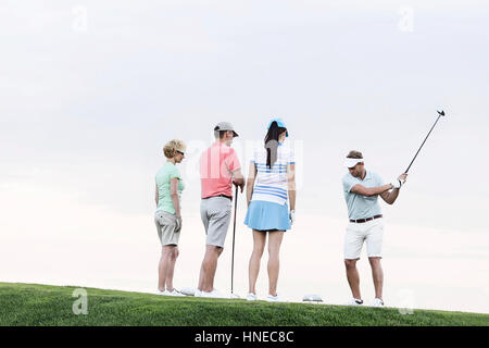 Group of friends looking at man playing golf against clear sky Stock Photo