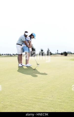 Full length of couple playing golf at course against clear sky Stock Photo
