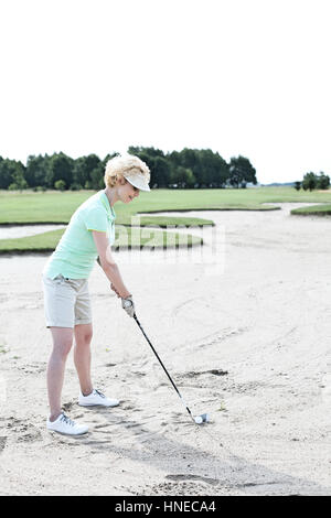 Middle-aged woman playing golf at course against clear sky Stock Photo