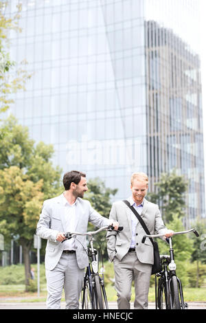 Businessmen with bicycles walking against office building