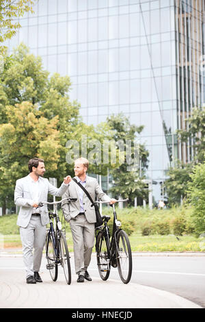 Businessmen talking while walking with bicycles on street