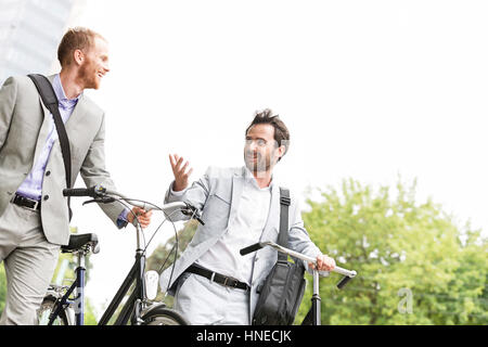 Businessmen talking while walking with bicycles outdoors