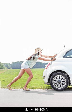 Full-length of woman pushing broken down car on country road Stock Photo