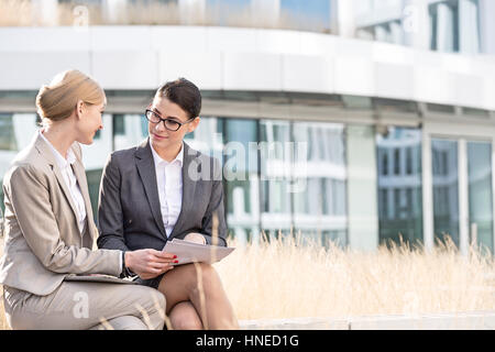 Businesswomen discussing over documents while sitting outside office building Stock Photo