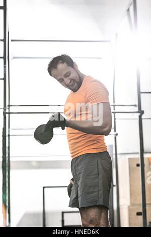 Confident man lifting kettlebell in crossfit gym Stock Photo