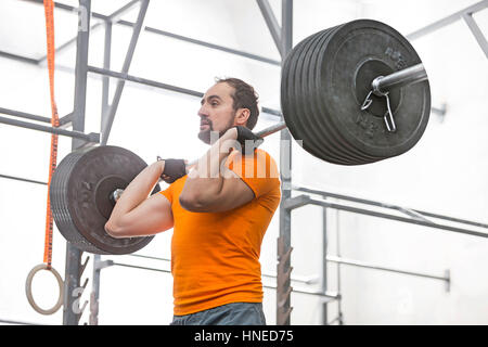 Confident man looking away while lifting barbell in crossfit gym Stock Photo