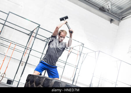 Man hitting tire with sledgehammer in crossfit gym Stock Photo