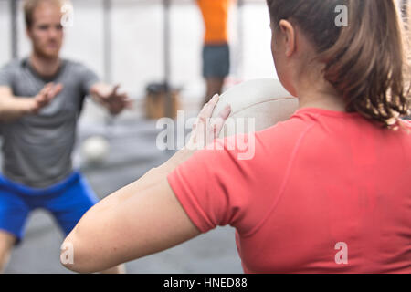 Rear view of woman throwing medicine ball towards man in crossfit gym Stock Photo