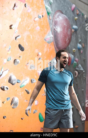 Dedicated man shouting by climbing wall in crossfit gym Stock Photo