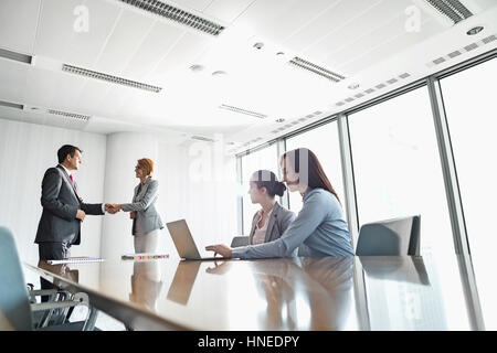 Businesspeople shaking hands in board room Stock Photo