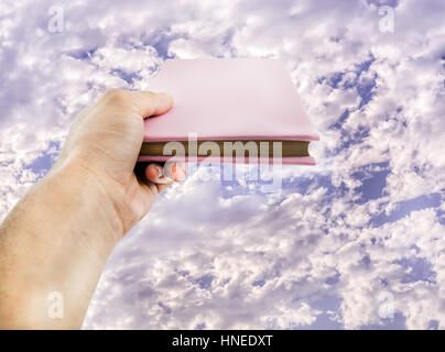 cloudy blue sky over a hand  holding a book .conceptual photo of cloud storage. online libraries and shopping  of books.holy book with copy space. Stock Photo