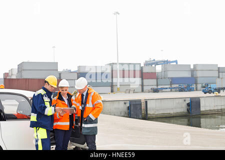 Workers using tablet PC beside car in shipping yard Stock Photo