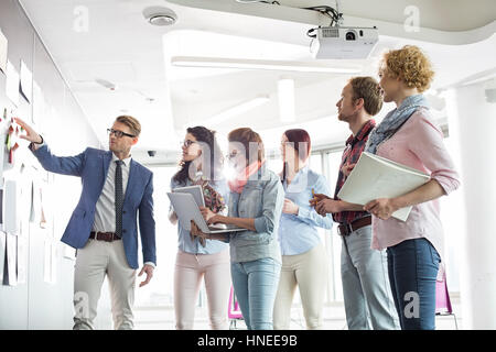 Businesspeople discussing over documents on wall in creative office Stock Photo