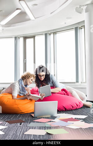 Businesswomen using tablet PC while relaxing on beanbag chairs at creative office Stock Photo