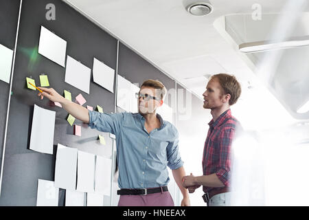 Creative businessmen discussing over sticky paper on wall in office Stock Photo