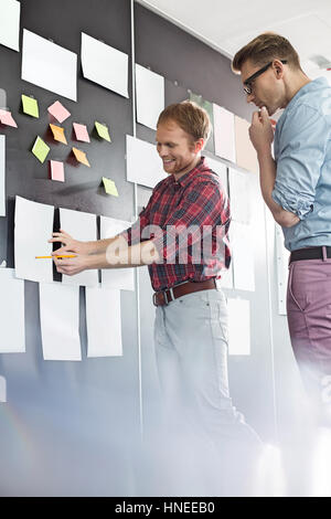 Creative businessmen discussing over document on wall in office Stock Photo