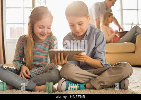 Happy siblings using digital tablet on floor with parents in background Stock Photo