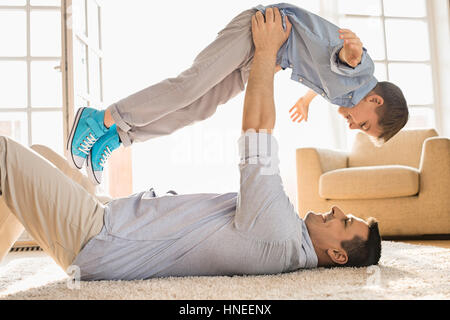 Side view of playful father lifting son while lying on floor at home Stock Photo