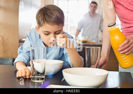 Midsection of woman with juice bottle standing by son having breakfast with man in background Stock Photo