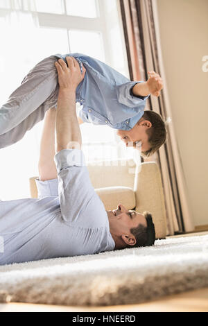 Side view of playful father picking up son while lying on floor at home Stock Photo