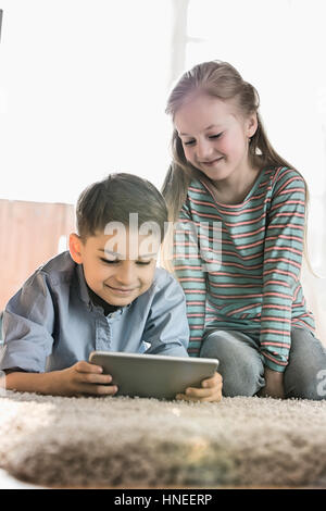 Siblings using digital tablet on floor at home Stock Photo