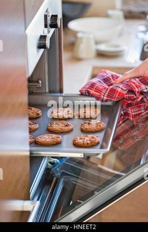 Cropped image of woman's hand removing cookie tray from oven in kitchen Stock Photo