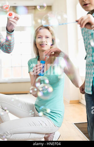 Happy mother and children playing with bubble wands at home Stock Photo