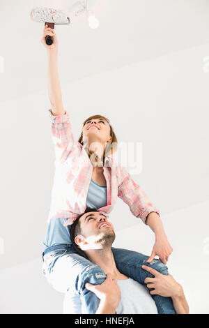 Woman on man's shoulders painting ceiling with paint roller Stock Photo