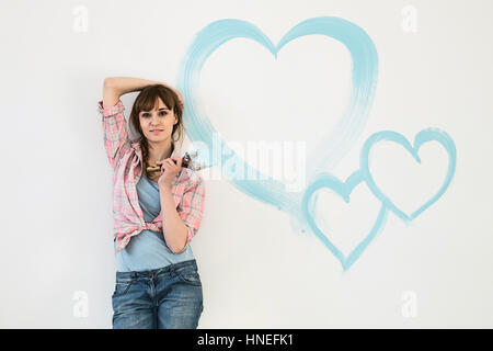 Portrait of beautiful woman holding paint brush with hearts painted on wall Stock Photo