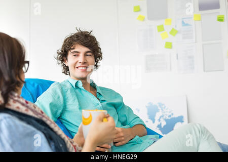 Businesspeople having coffee while relaxing on beanbag chairs in creative office Stock Photo