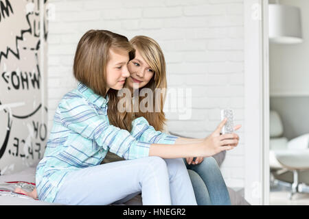 Cute sisters photographing themselves through cell phone at home Stock Photo