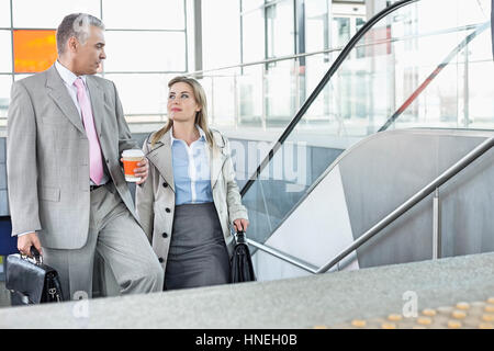 Businessman conversing with female colleague while walking up stairs in train station Stock Photo