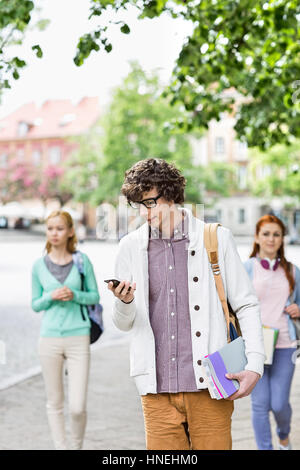 Young male student using cell phone with friends in background on street Stock Photo