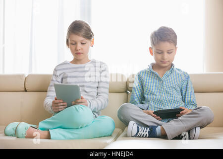 Cute siblings using technologies on sofa at home Stock Photo