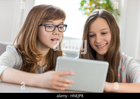 Sisters using digital tablet at table in house Stock Photo