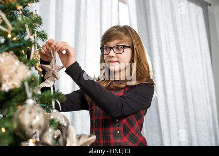 Teenage girl hanging ornament on Christmas tree at home