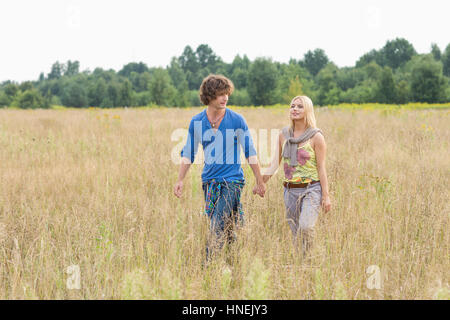 Young couple holding hands while walking through field Stock Photo