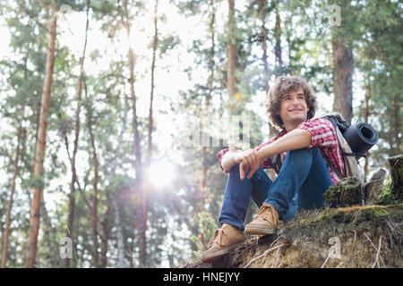 Full length of smiling male hiker looking away while sitting on cliff in forest Stock Photo