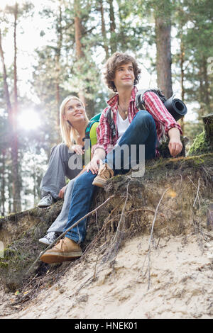 Full length of hiking couple sitting on edge of cliff in forest Stock Photo