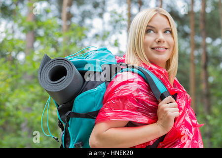 Side view smiling female backpacker in raincoat looking away at forest Stock Photo