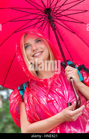 Smiling female hiker in red raincoat holding umbrella Stock Photo